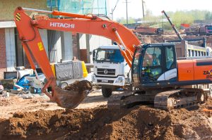 Orange Hitachi excavator digging at a construction site with trucks and equipment nearby.