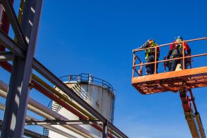 Industrial workers inspecting equipment on a lift at a construction site under a clear blue sky.
