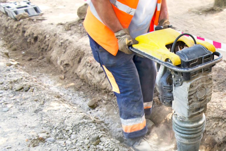 Construction worker operating a compactor on a dirt construction site.
