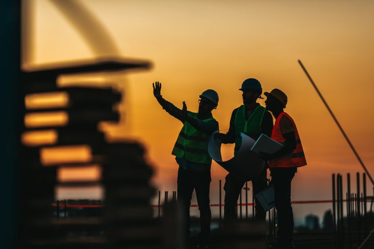Construction site workers discussing plans at sunset with safety gear.