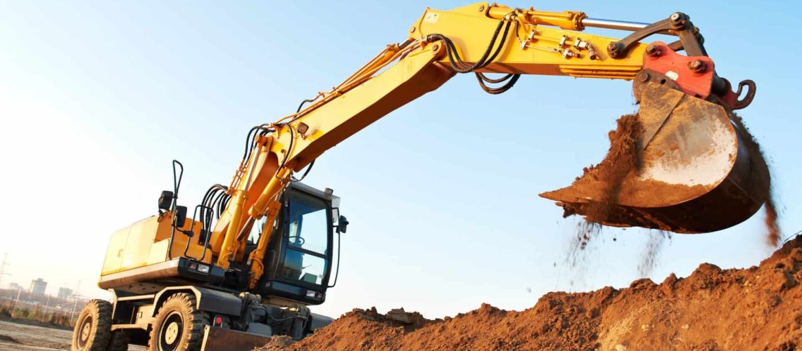Heavy yellow excavator digging earth at construction site with blue sky background.