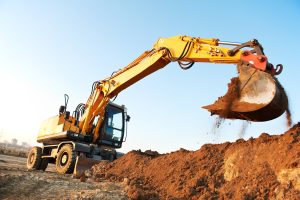 Heavy yellow excavator digging earth at construction site with blue sky background.