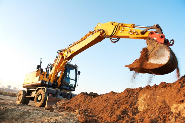 Heavy yellow excavator digging earth at construction site with blue sky background.
