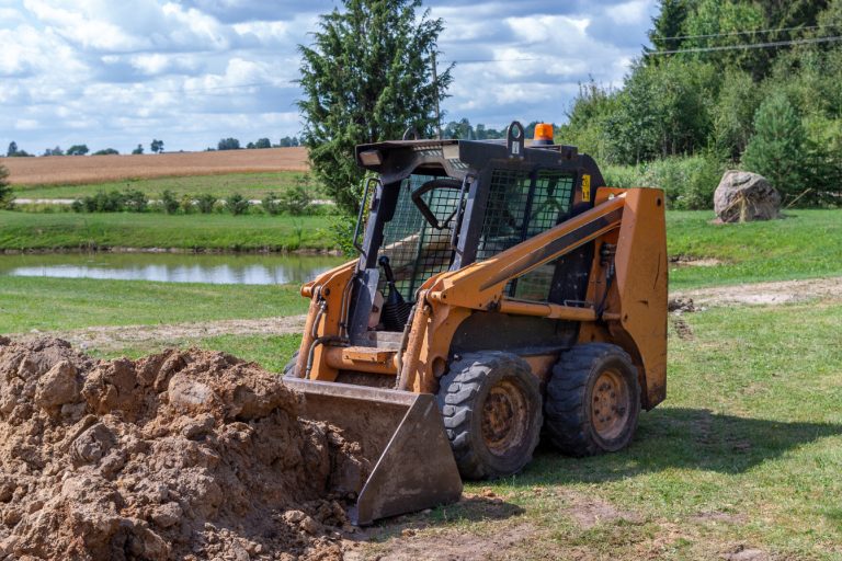 Excavator digging soil on a construction site with a rural landscape background.